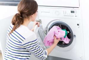 Junge Frau legt Wäsche in Waschmaschine